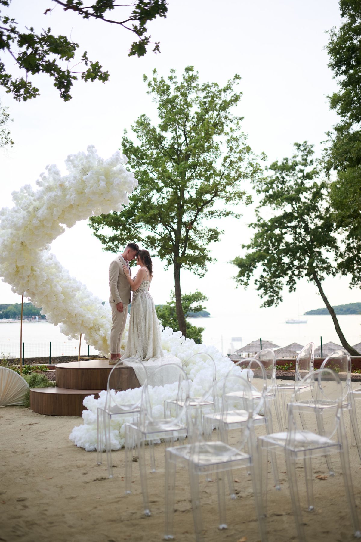 Bride and groom under a white floral arch by the sea at D'Orangerie, Istria